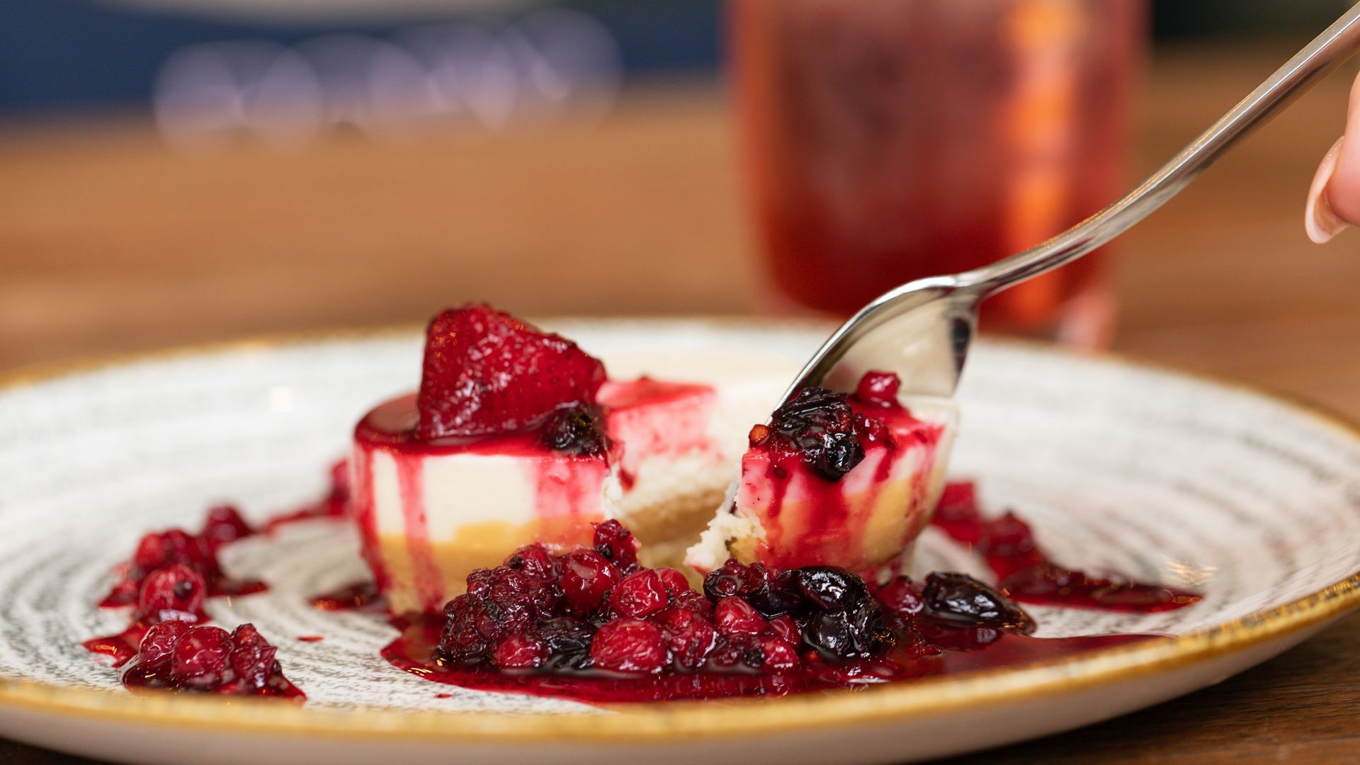 Cheesecake slice with berry compote, being eaten with a spoon, on a plate.