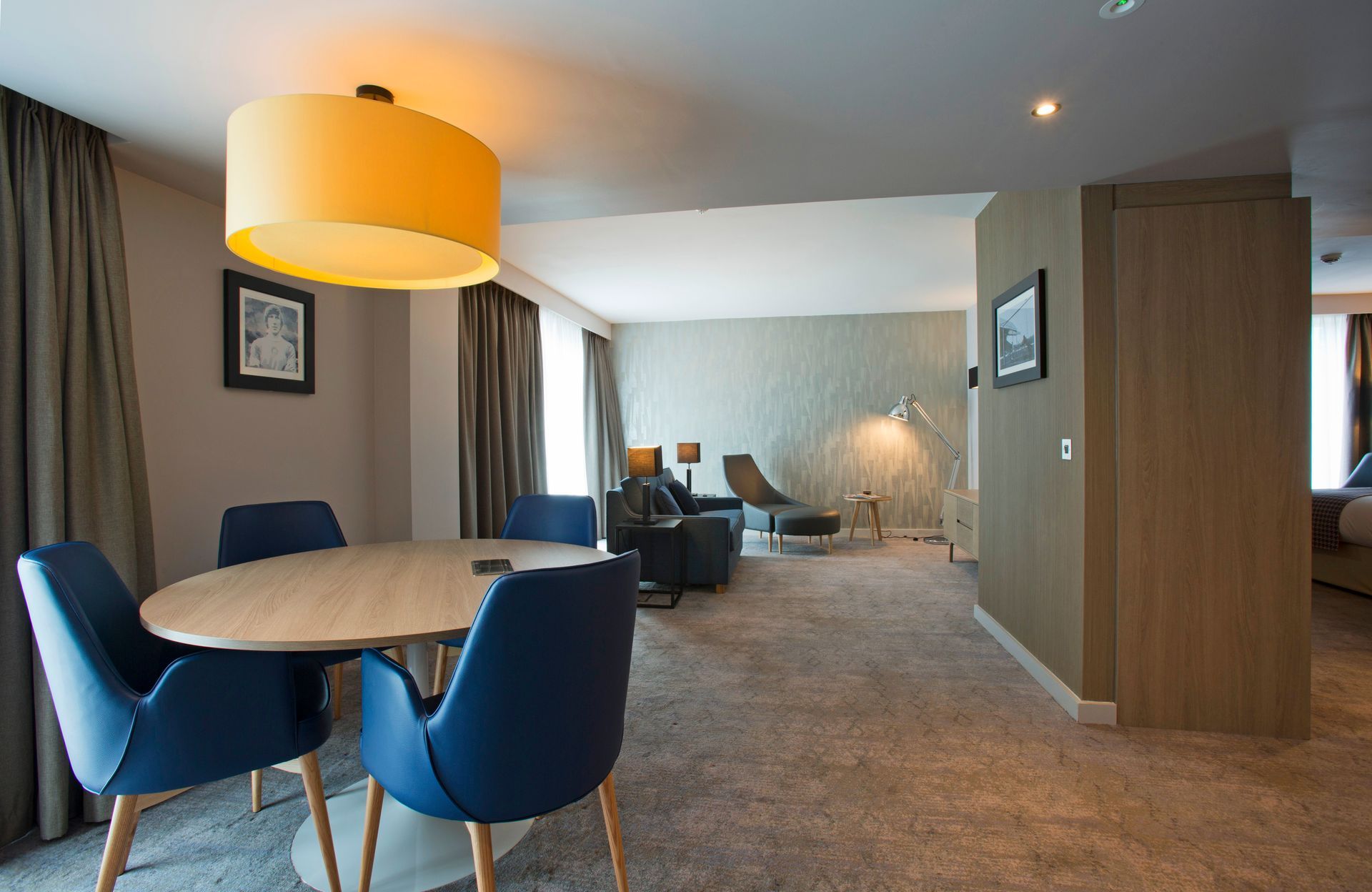 A hotel suite with a dining area, living room, and bedroom. Blue chairs surround a table.