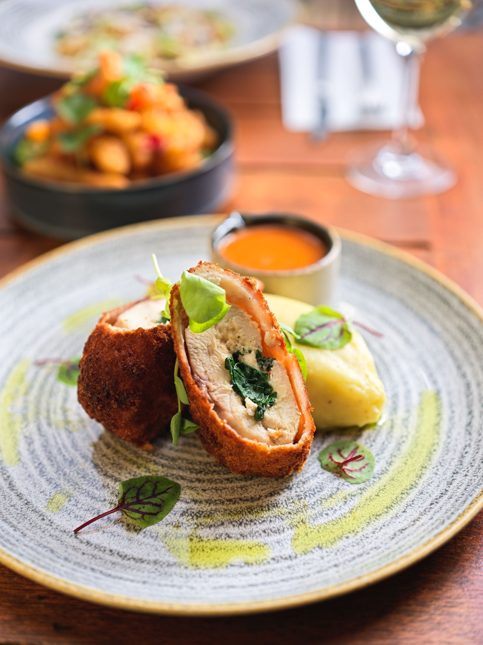 Breaded chicken roll with spinach, mashed potatoes, and sauce on a plate.