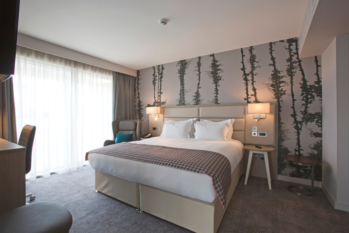 Hotel bedroom with a bed, patterned wallpaper, and large window.