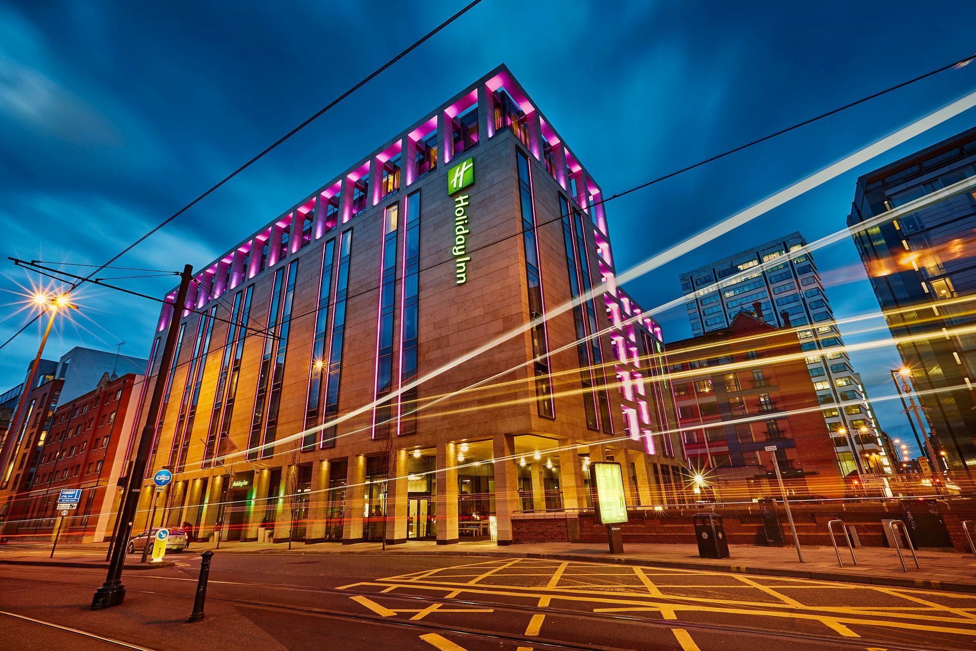 Night view of a Holiday Inn hotel with illuminated exterior, street scene with streaks of light.