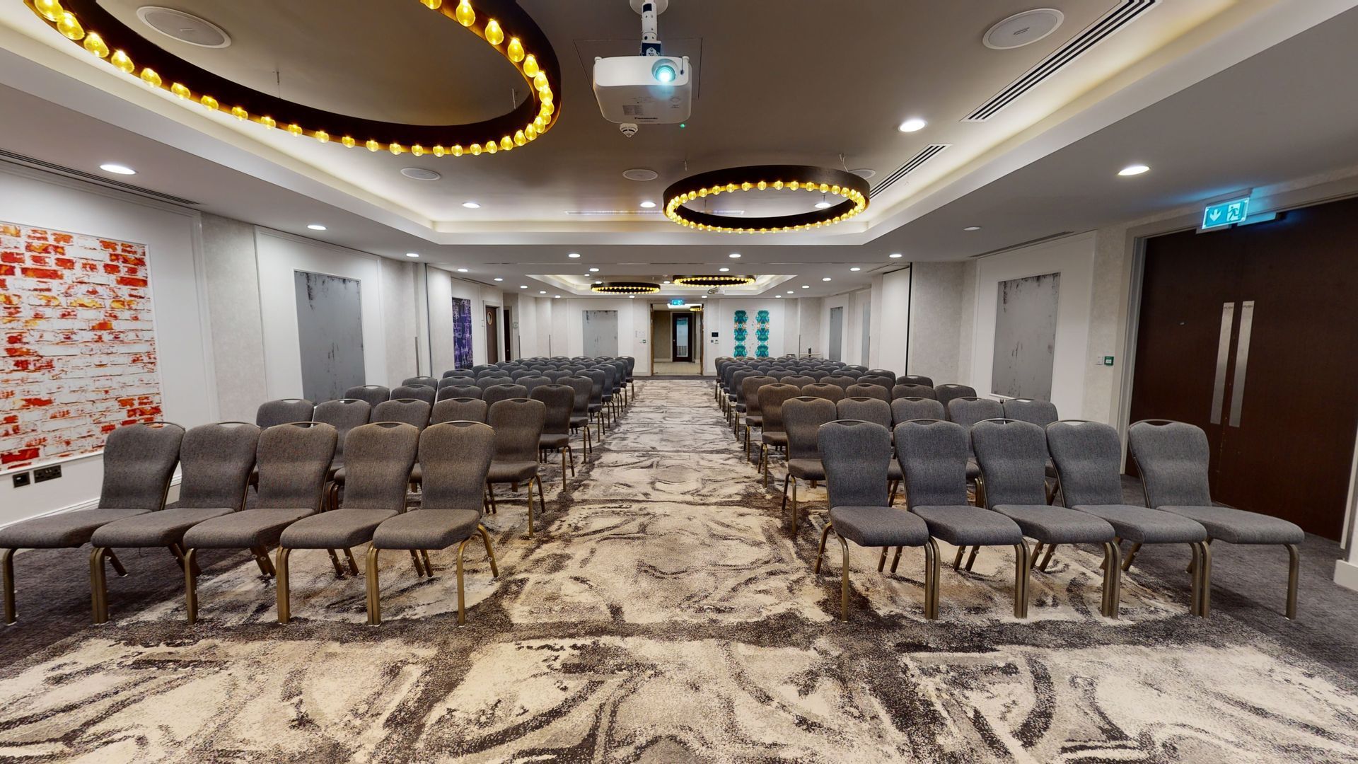 Conference room with rows of gray chairs, neutral carpet, and circular ceiling lights.