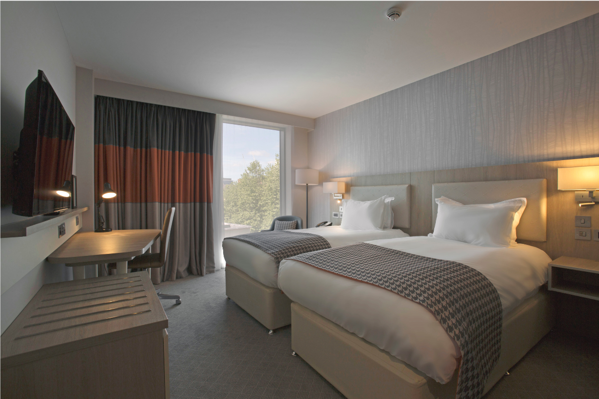 Hotel room with two twin beds, desk, and a window with neutral tones.