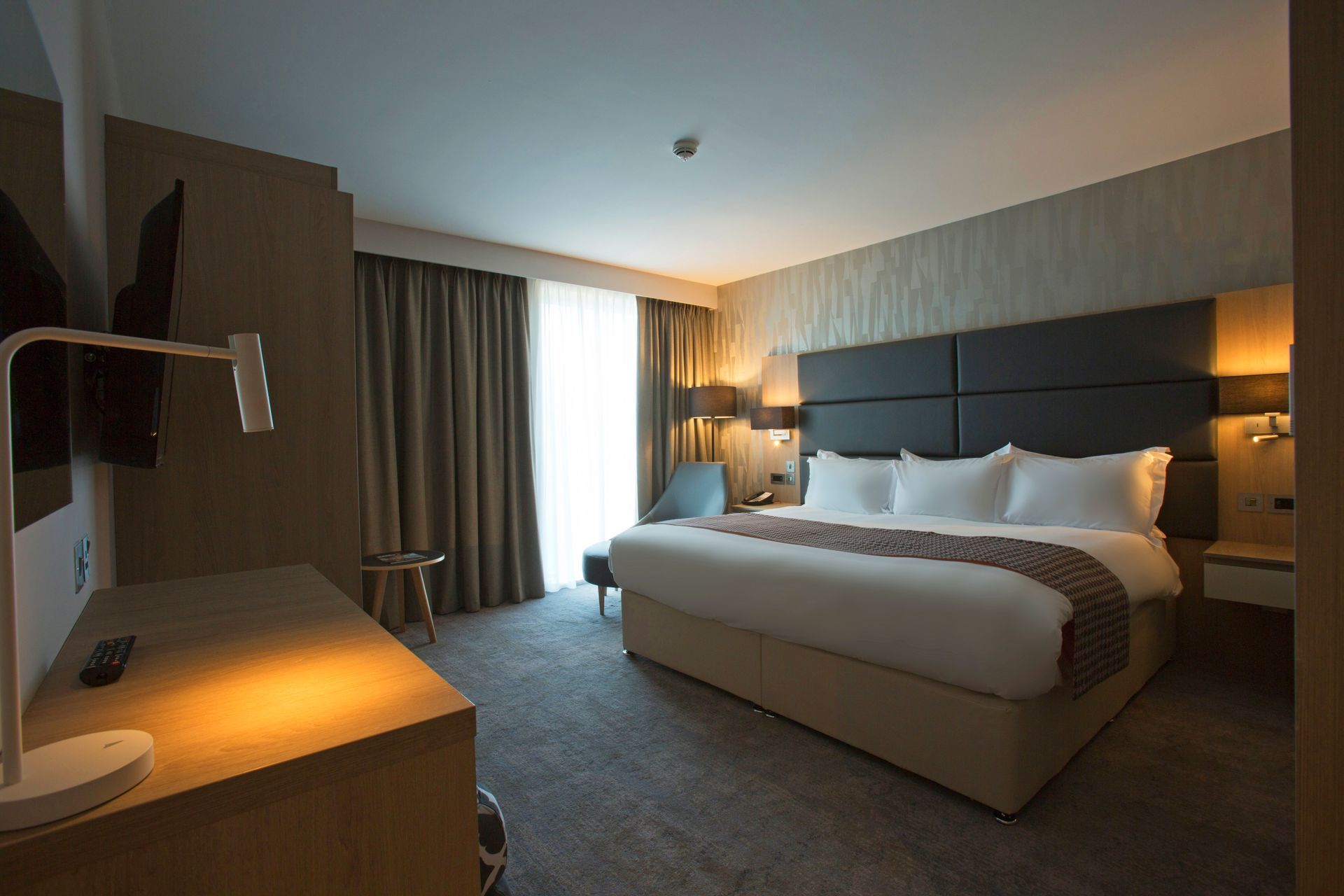 Hotel room with king-size bed, desk, window, and neutral colors.
