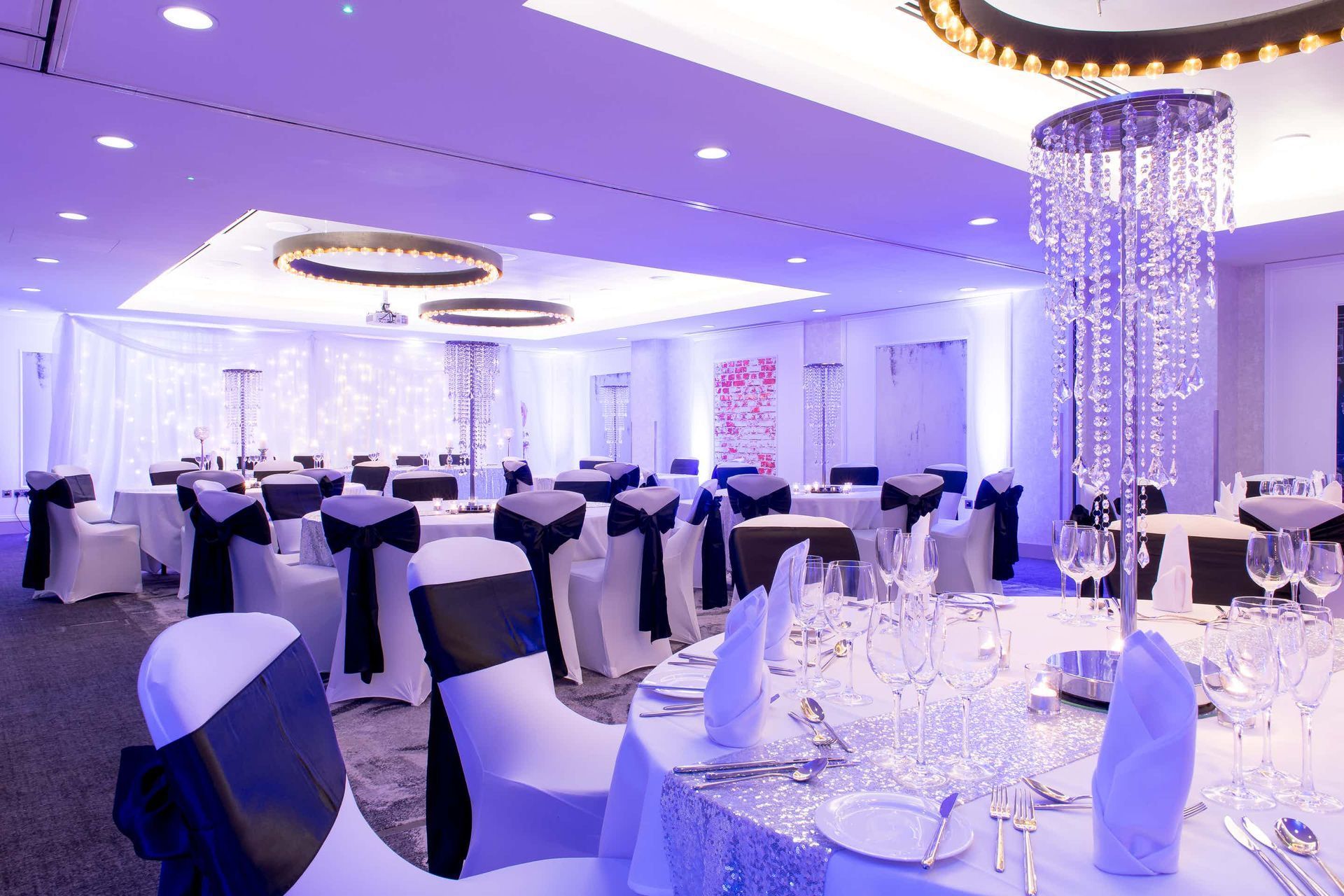 Elegant banquet hall with round tables, white and black decor, and a large chandelier.