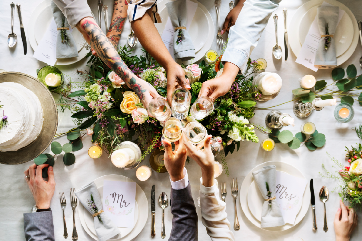 People toasting at a wedding reception. Floral centerpiece, cake, place settings, and candles adorn the table.