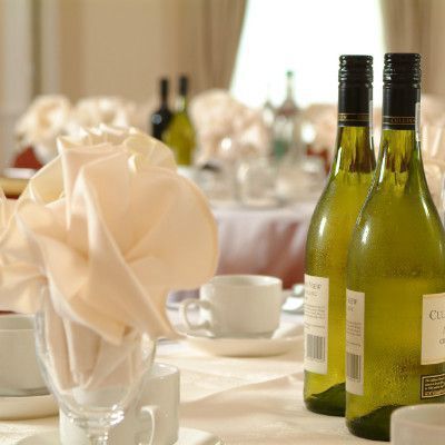 Table setting with folded napkin, wine bottles, and cups, likely at a catered event.