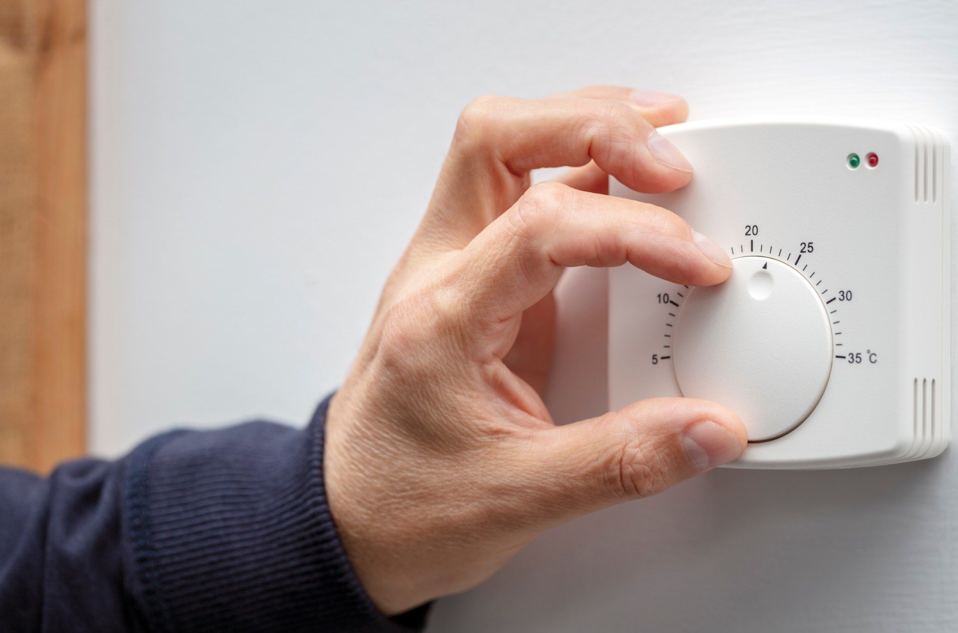 Eine Person stellt einen Thermostat an einer Wand ein.