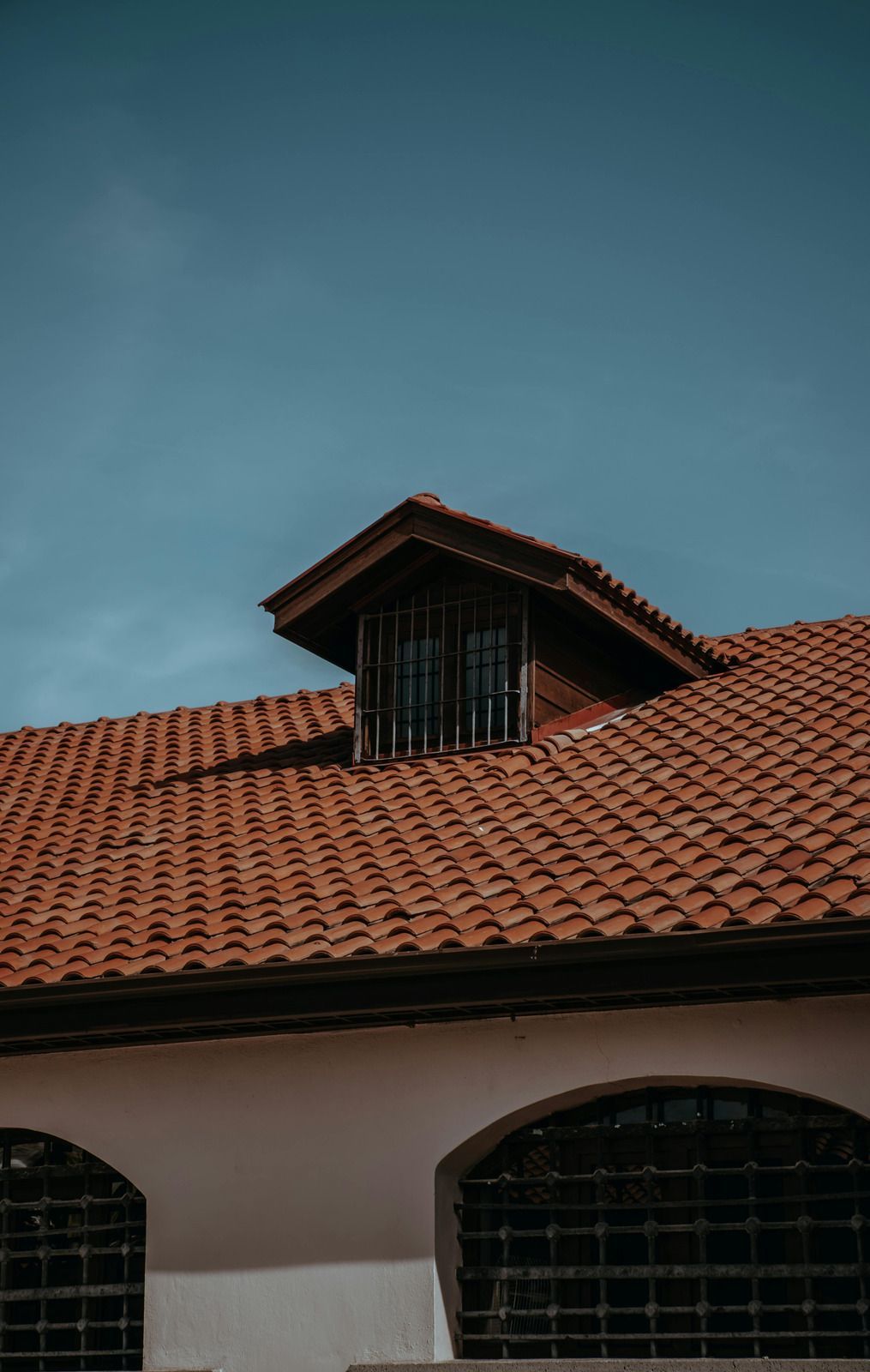 Red-tiled roof with a dormer against a blue sky above an arched building facade