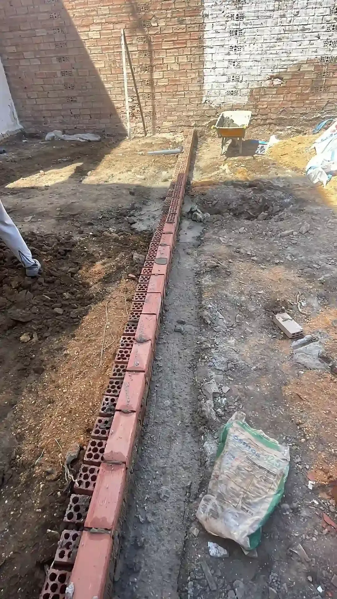 Zanja de una obra en construcción con una estrecha hilera de ladrillos rojos