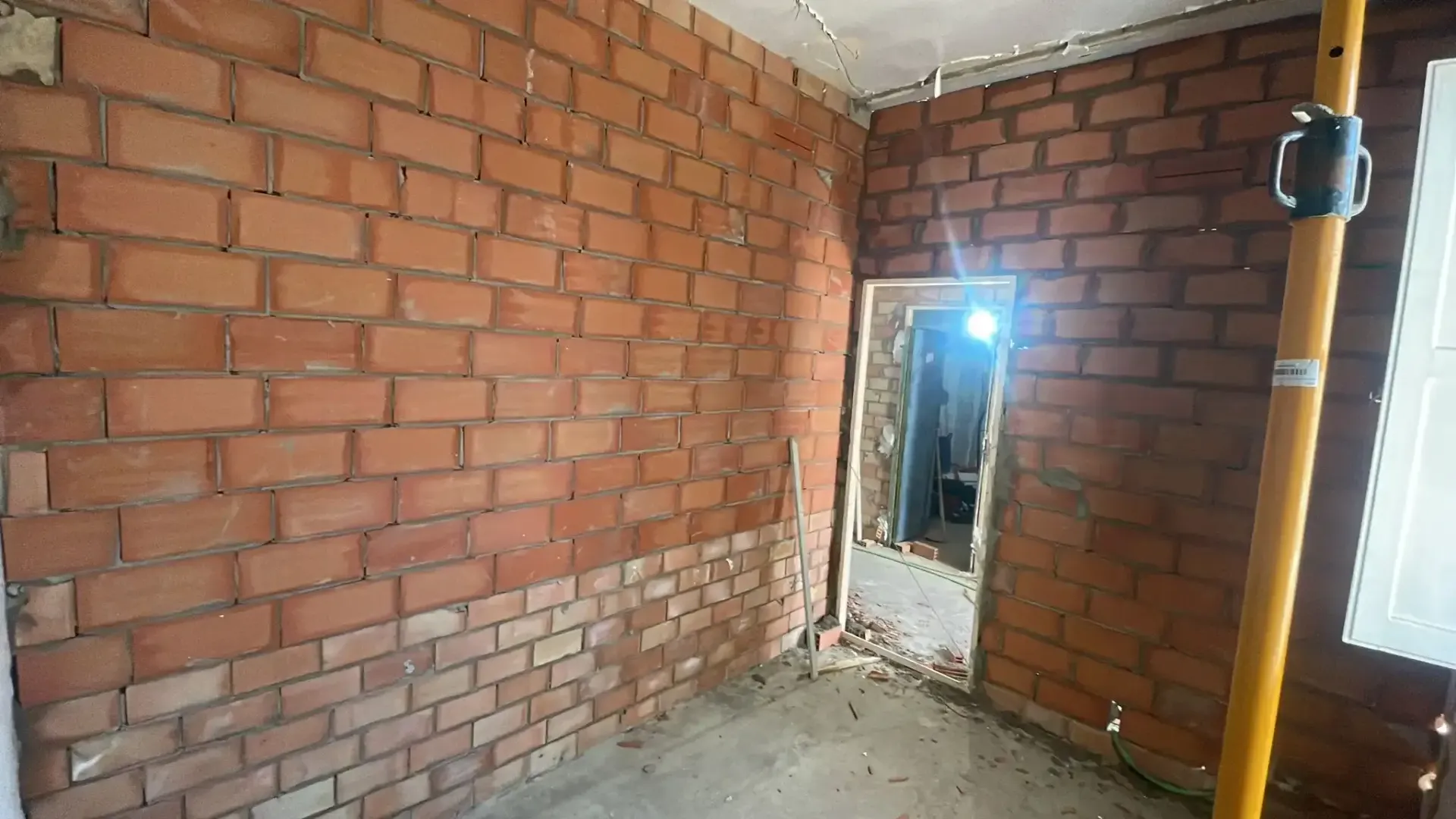 Interior de ladrillo sin terminar con una puerta que da a una habitación luminosa