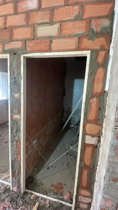 Muro de ladrillo sin terminar con una puerta tosca que da a un interior oscuro en construcción.