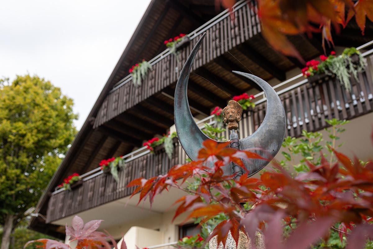 Balkon mit roten Blumenkästen und einer großen Mondsichel-Skulptur vor einem Chalet