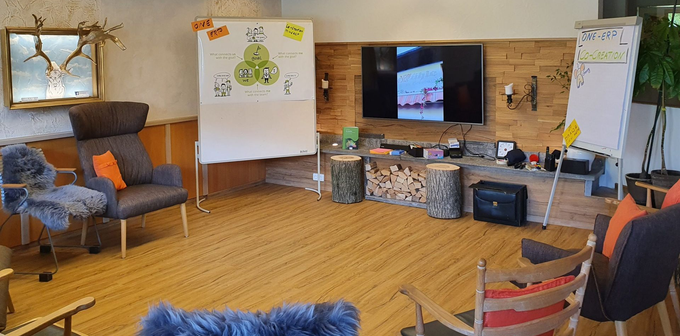 Gemütliches Wohnzimmer mit Sesseln, Fernseher an einer Holzwand, Whiteboards und Regalen neben dem Kamin.