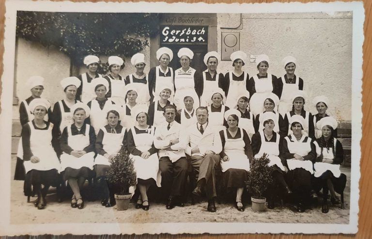 Formelles Gruppenporträt von Pflegekräften in weißen Uniformen und Hauben, die vor einem Gebäude im Freien posieren
