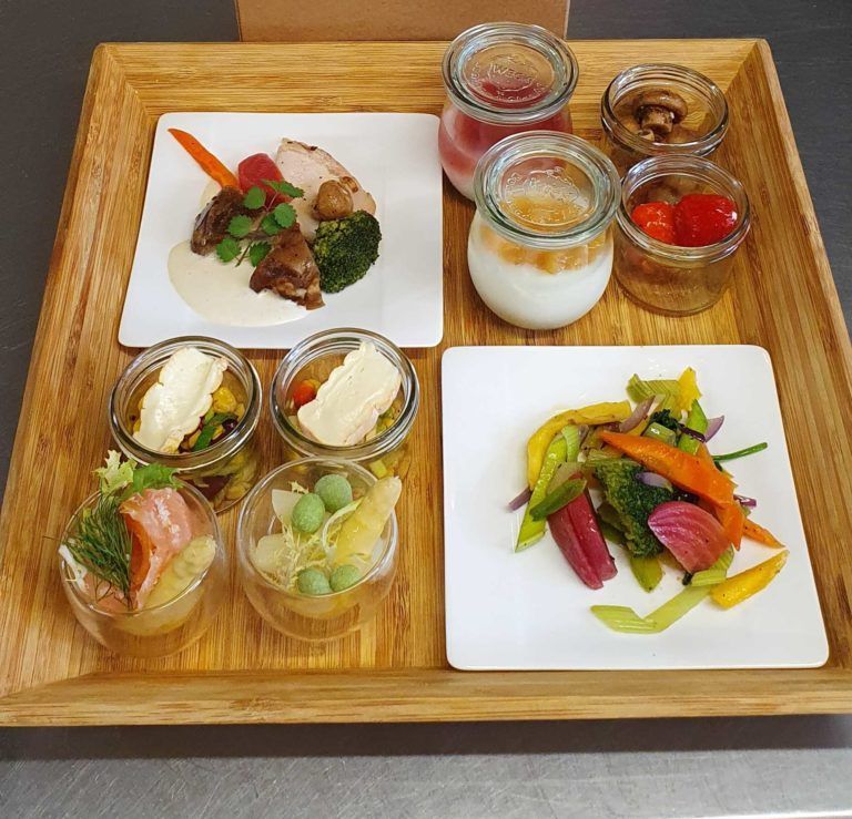 Holztablett mit einer Auswahl an bunten Gourmet-Häppchen und kleinen Gläsern mit Saucen und Desserts