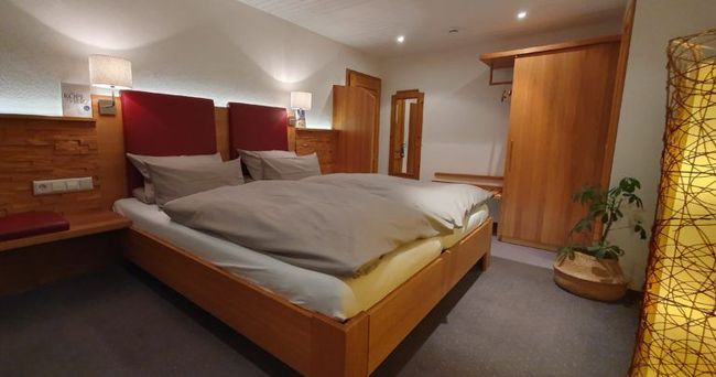 Gemütliches Schlafzimmer mit einem Holzbett, grauer Bettwäsche, warmem Licht und Kleiderschränken