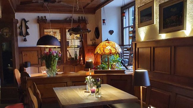 Gemütliches, gedämpft beleuchtetes Café oder Lounge mit Holzvertäfelung, Tischlampen, Blumen und einem Tischgesteck.