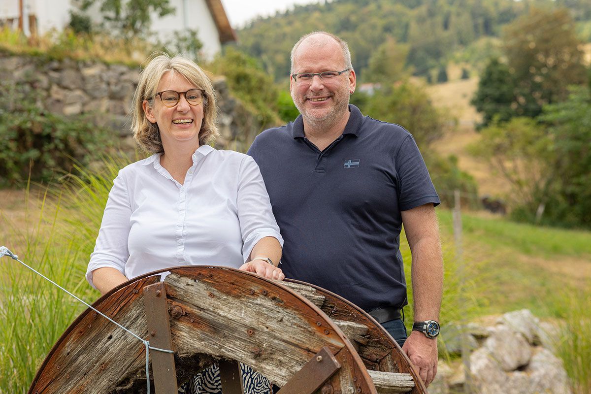 Zwei Personen stehen hinter einem rostigen Rad in einem grünen Garten auf dem Land