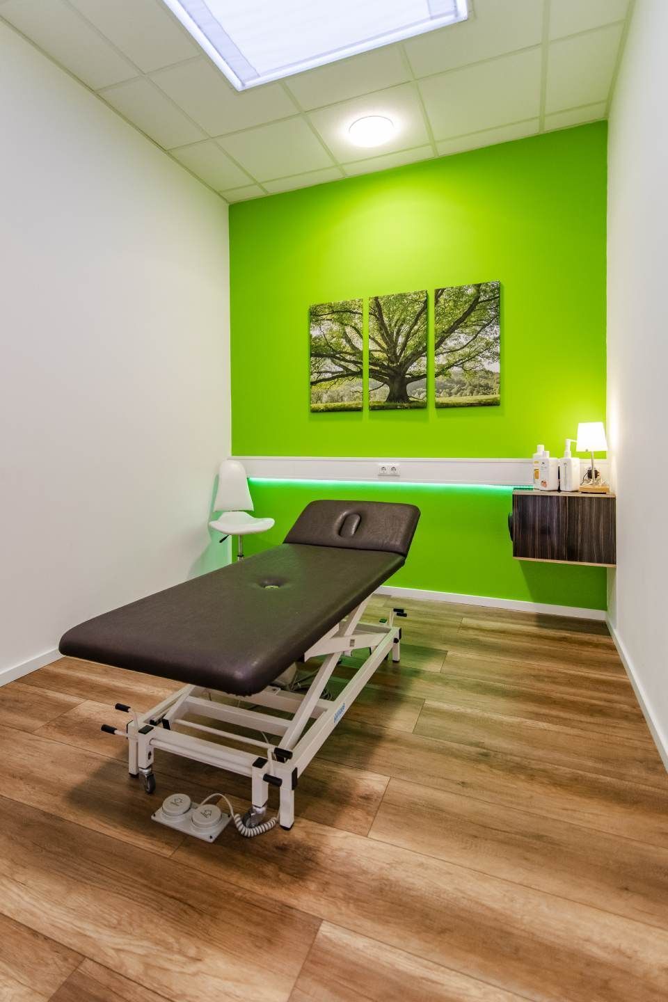 Ein Untersuchungsraum mit Massageliege, limettengrüner Akzentwand und Holzbodenoptik.