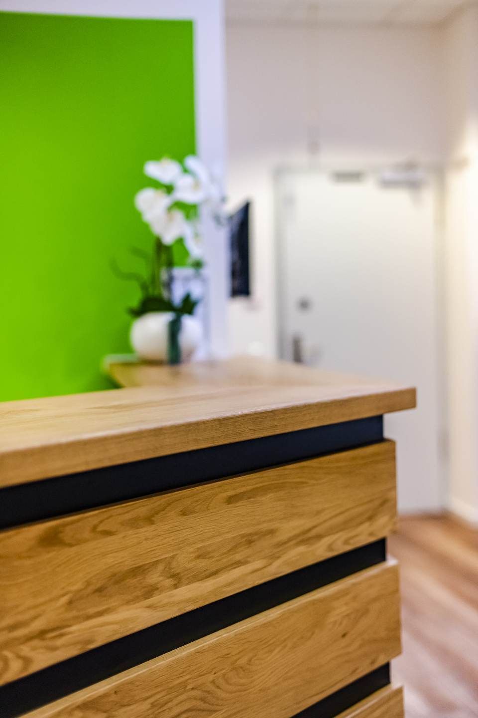 Empfangstresen aus Holz vor einer weißen Orchidee und einer grünen Wand.