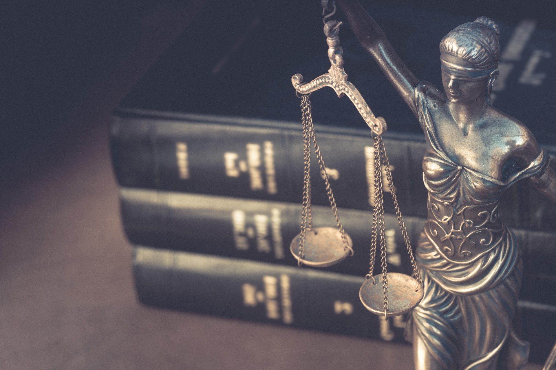 Eine Statue der Justitia, die vor einem Stapel Bücher die Waage der Gerechtigkeit hält.