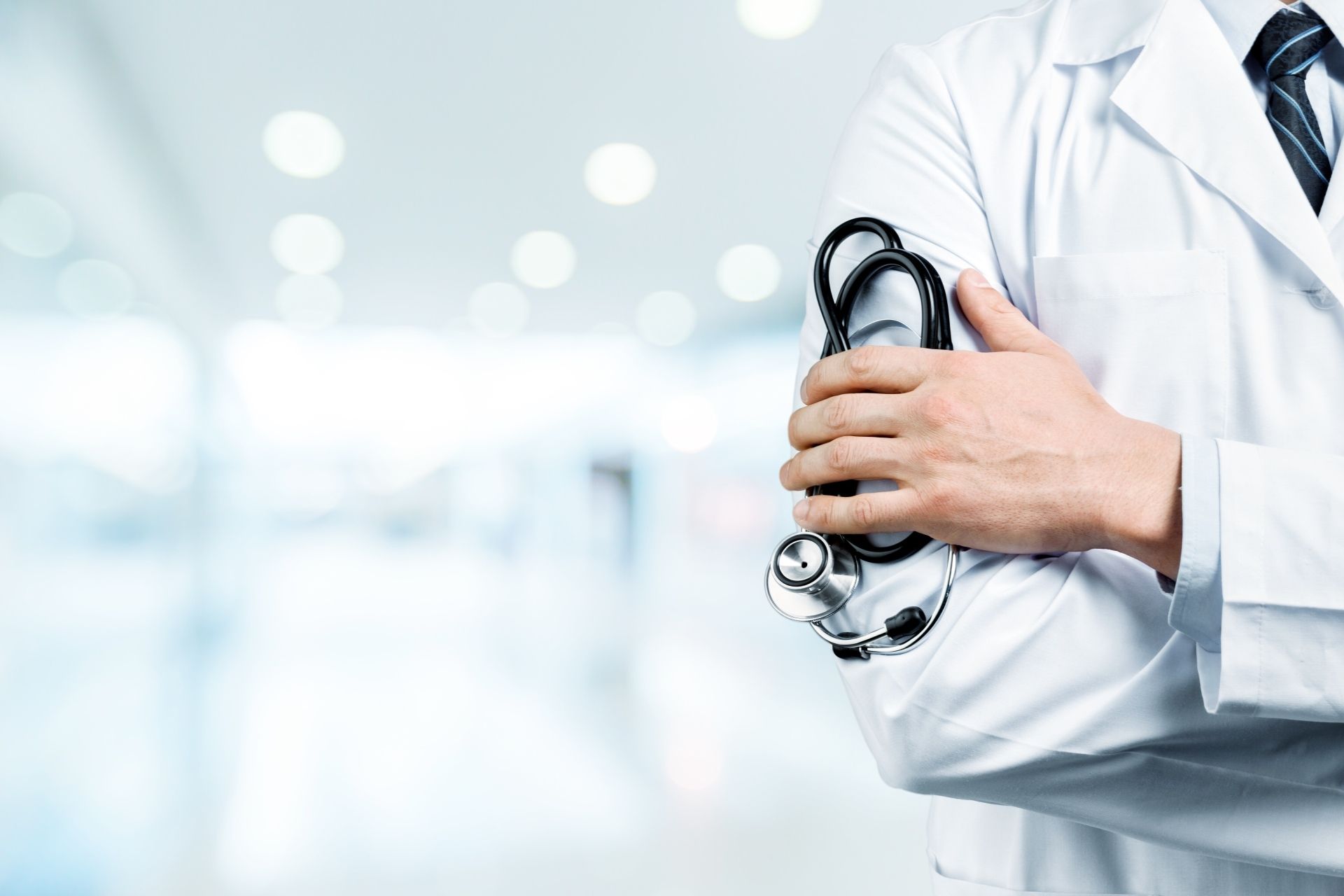 In einem Krankenhaus hält ein Arzt mit verschränkten Armen ein Stethoskop.