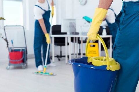 Un hombre sostiene un balde azul y un trapeador en una oficina.