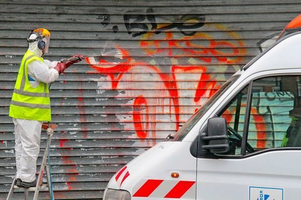 Un hombre está pintando grafitis con aerosol en la puerta de un garaje al lado de una camioneta blanca.