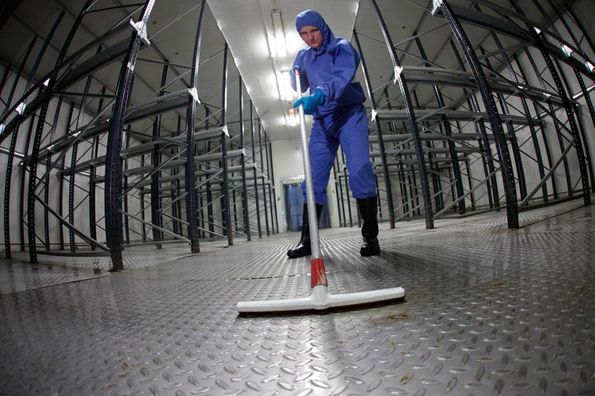 Un hombre con un traje azul está limpiando el piso de un almacén con un trapeador.
