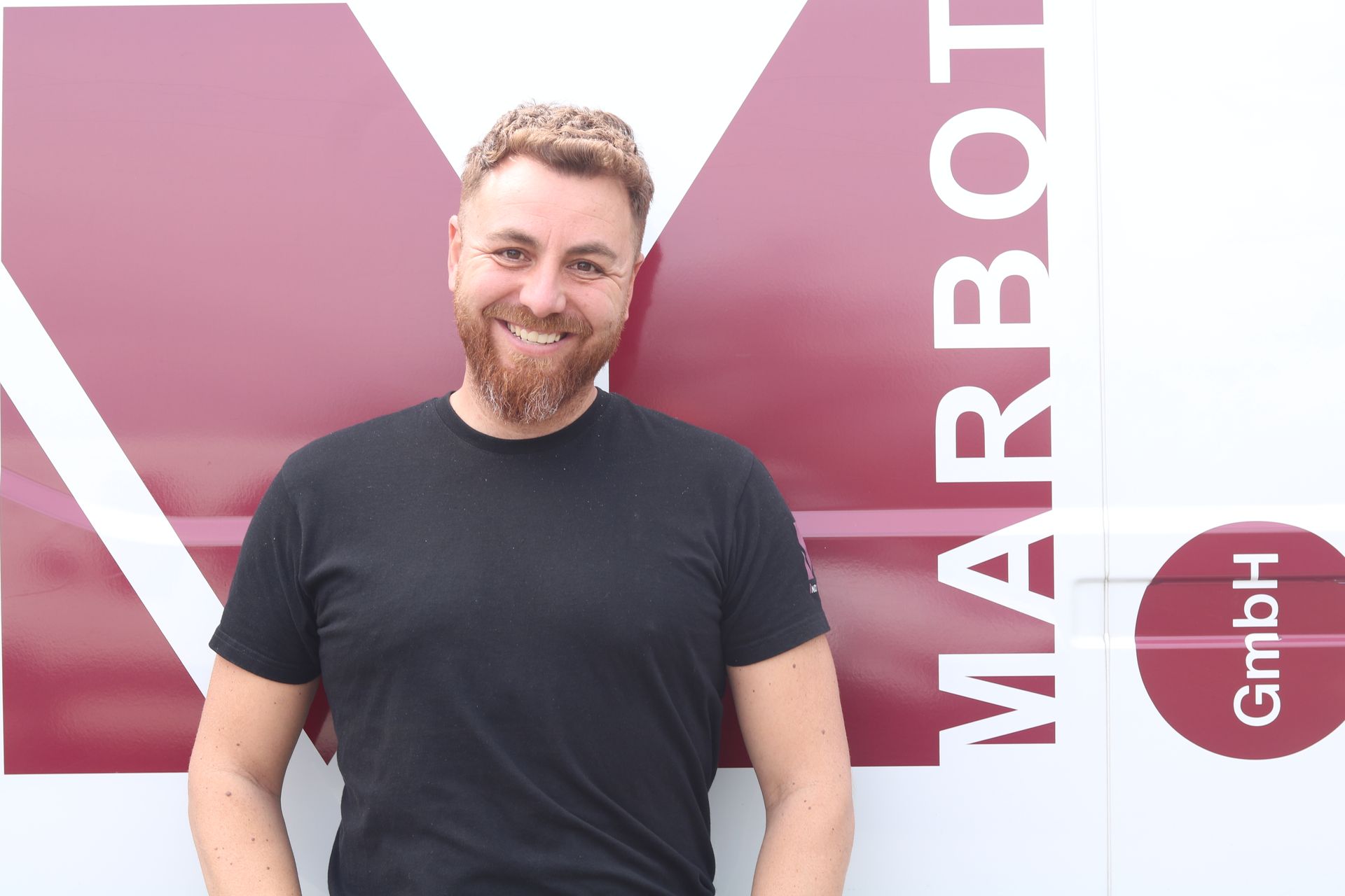 Ein Mann mit Bart steht vor einem rot-weißen Lieferwagen.