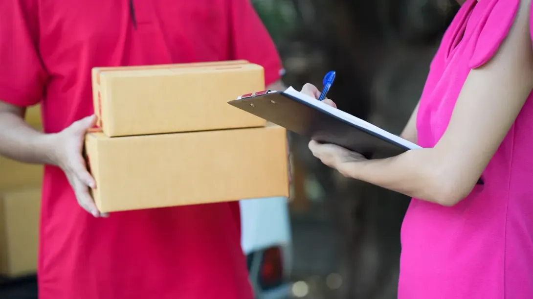 Un repartidor le entrega una caja a una mujer que sostiene un portapapeles.