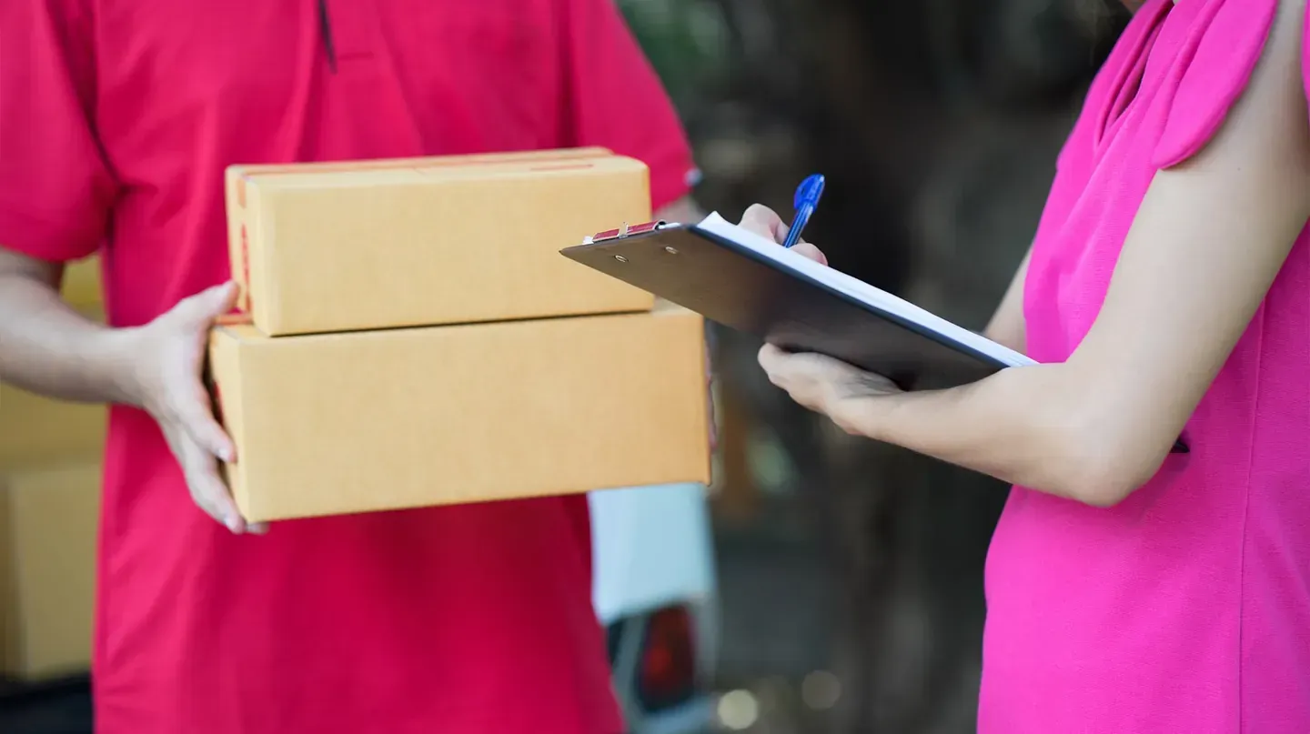 Un repartidor le entrega una caja a una mujer que sostiene un portapapeles.