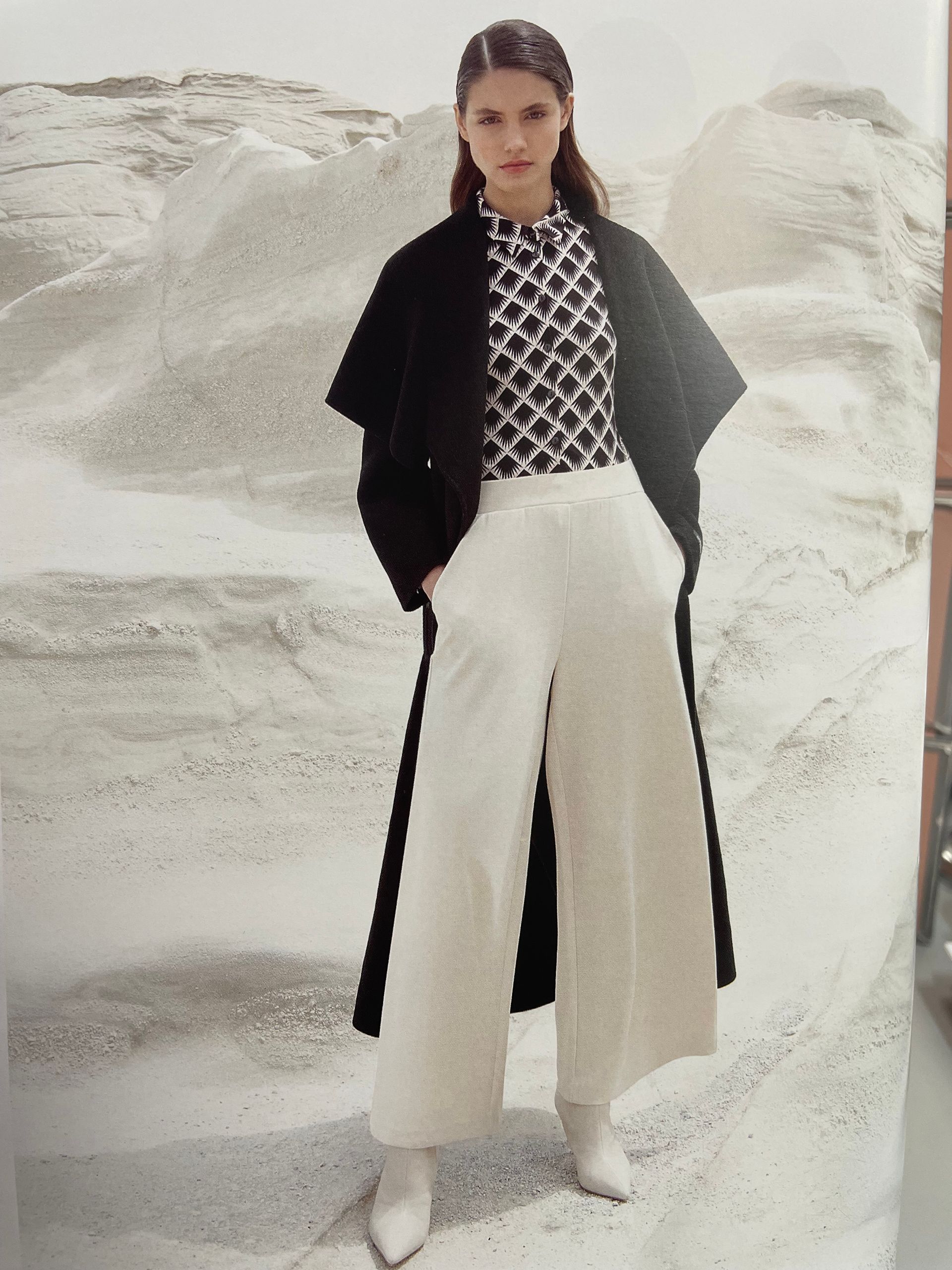 Manteau long noir, top à motifs noir et pantalon crème