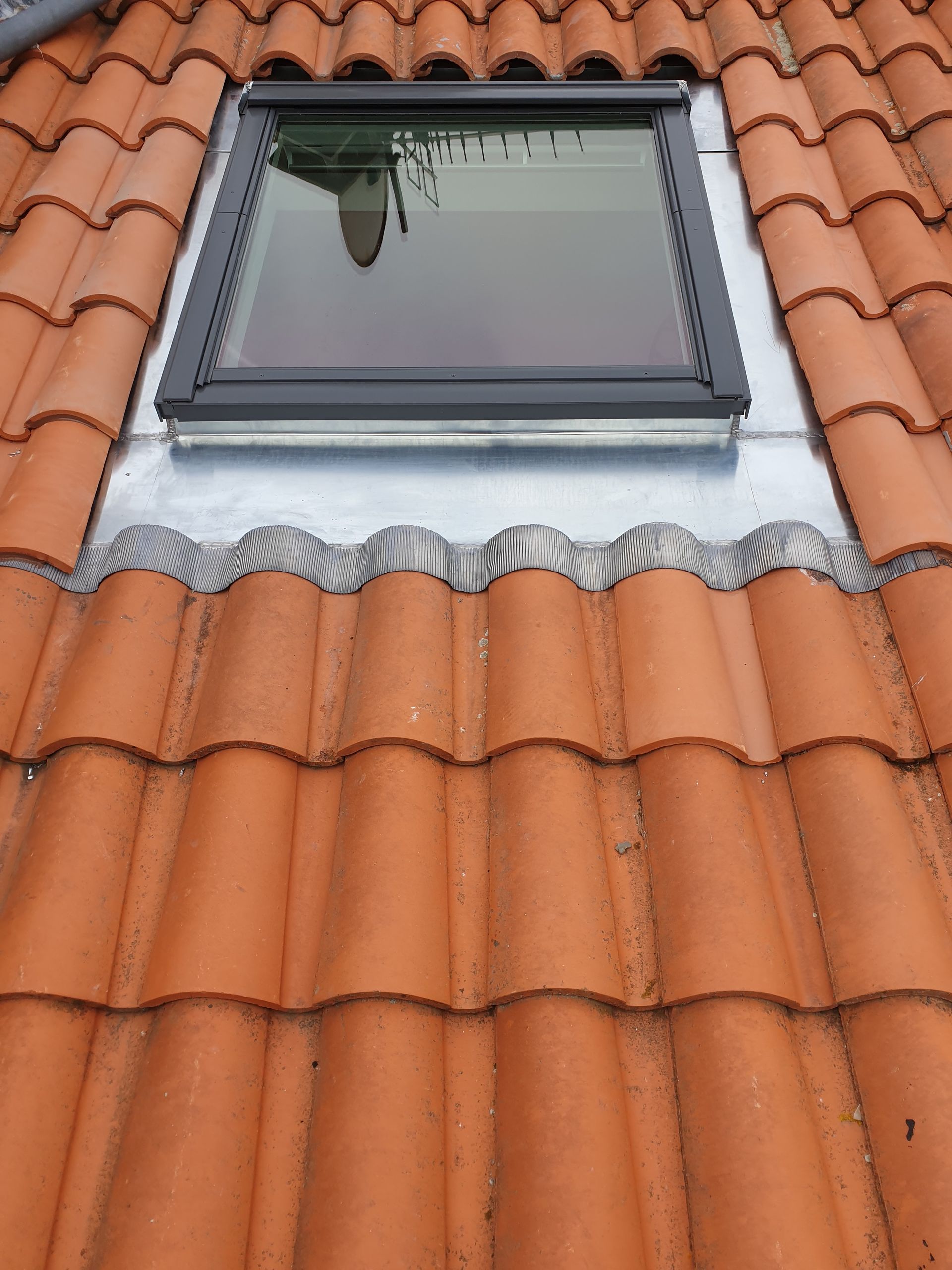 Puits de lumière avec solin gris, intégré à des tuiles en terre cuite orange.