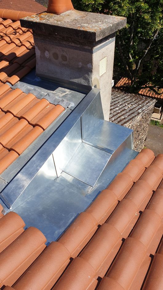 Cheminée de toit avec solin métallique brillant entre les tuiles en terre cuite.
