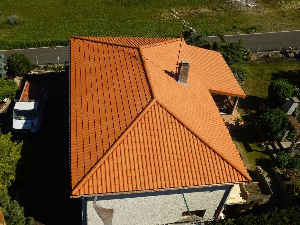 Vue en plongée d'un toit de tuiles en terre cuite sur une maison de couleur claire.