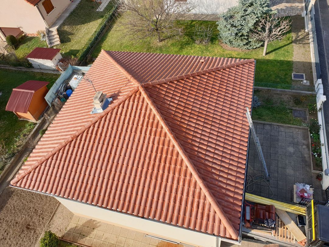 Vue en plongée d'une maison au toit à quatre pans de tuiles rouges, entourée d'une cour et d'un petit abri.