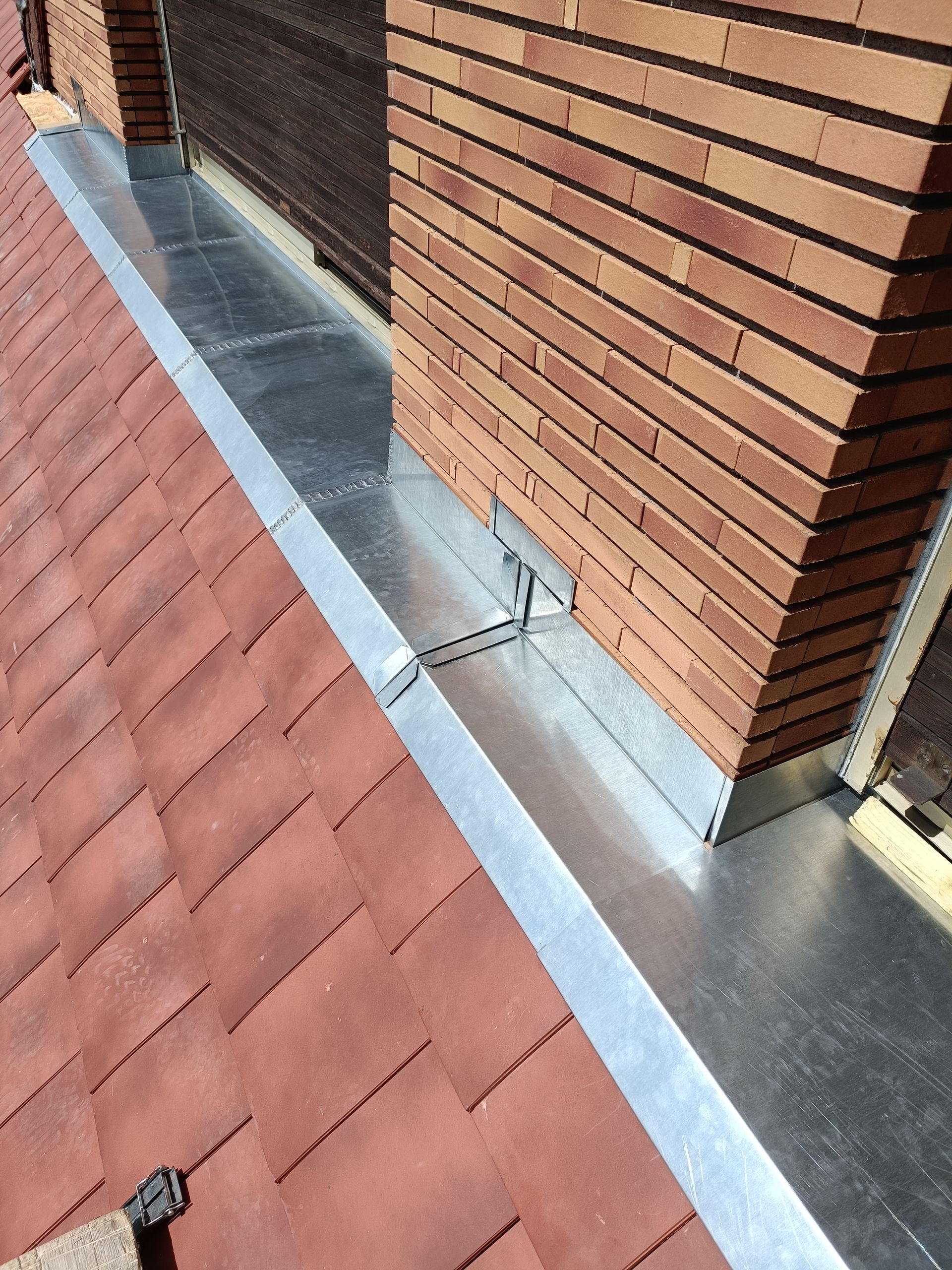 Cheminée de toit avec mur en briques, solins métalliques et tuiles rouges.