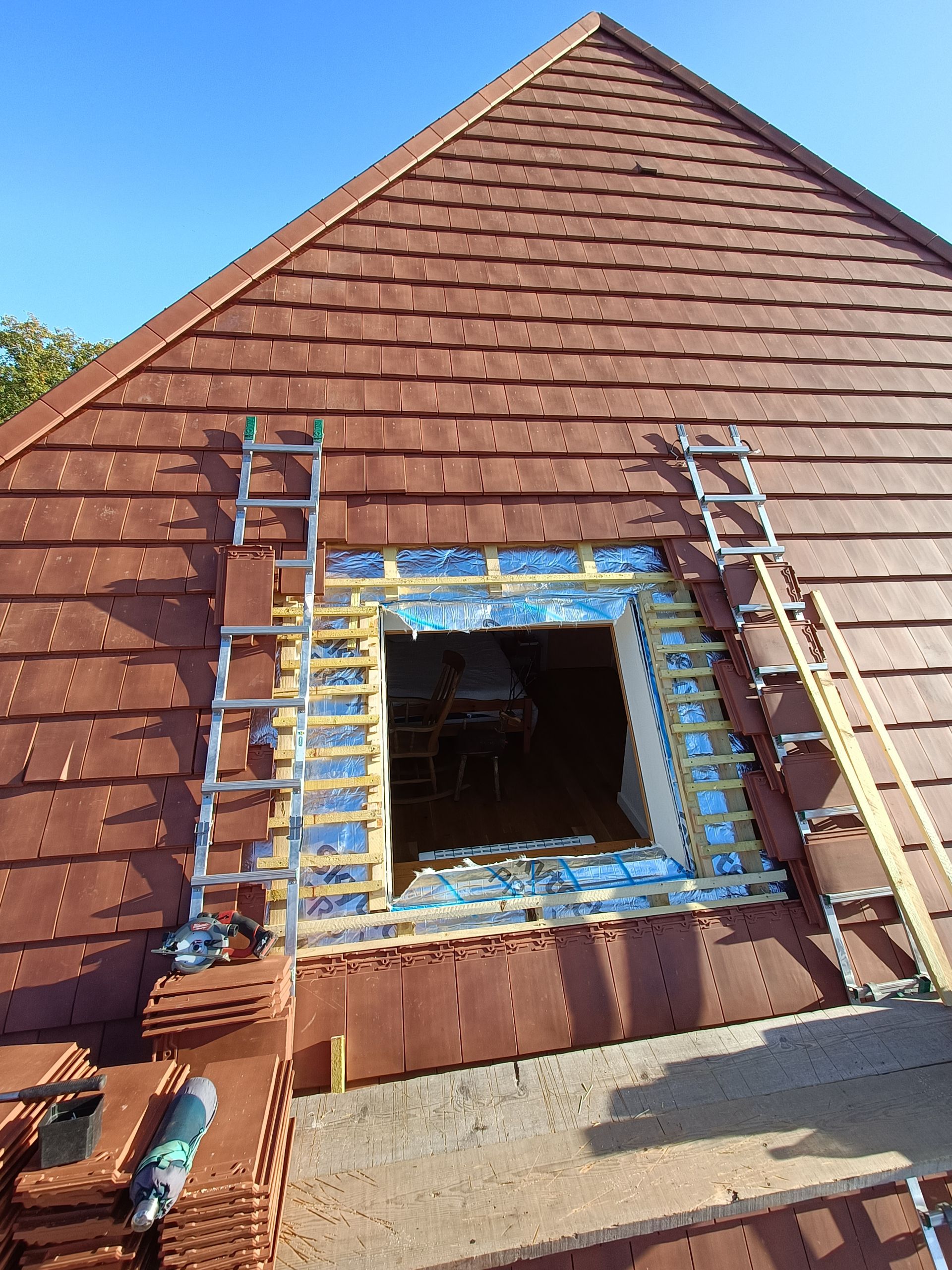 Toiture en réparation avec une lucarne, des échelles et une bordure de protection.