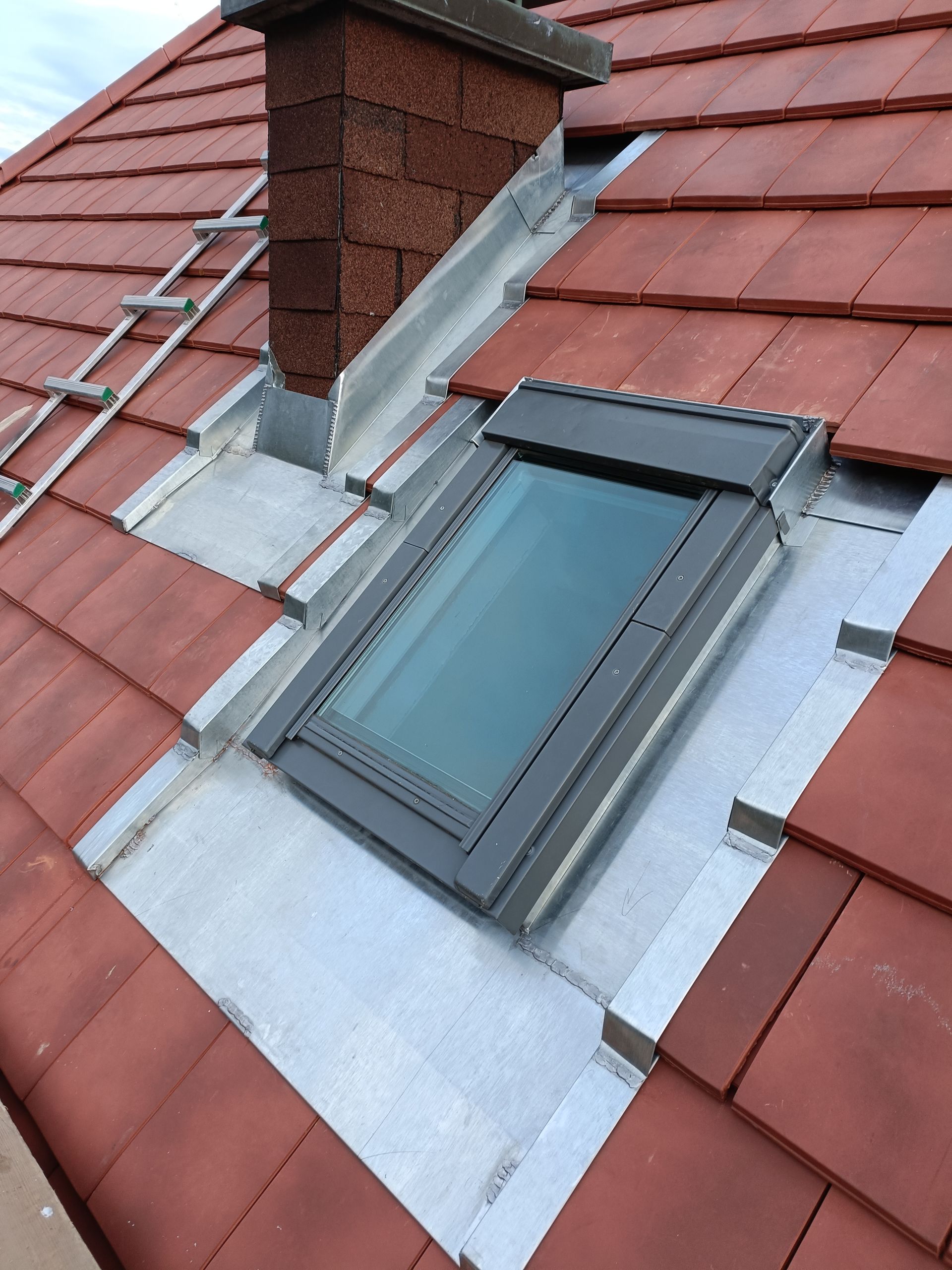 Puits de lumière avec solin gris entouré de tuiles rouges et cheminée en briques