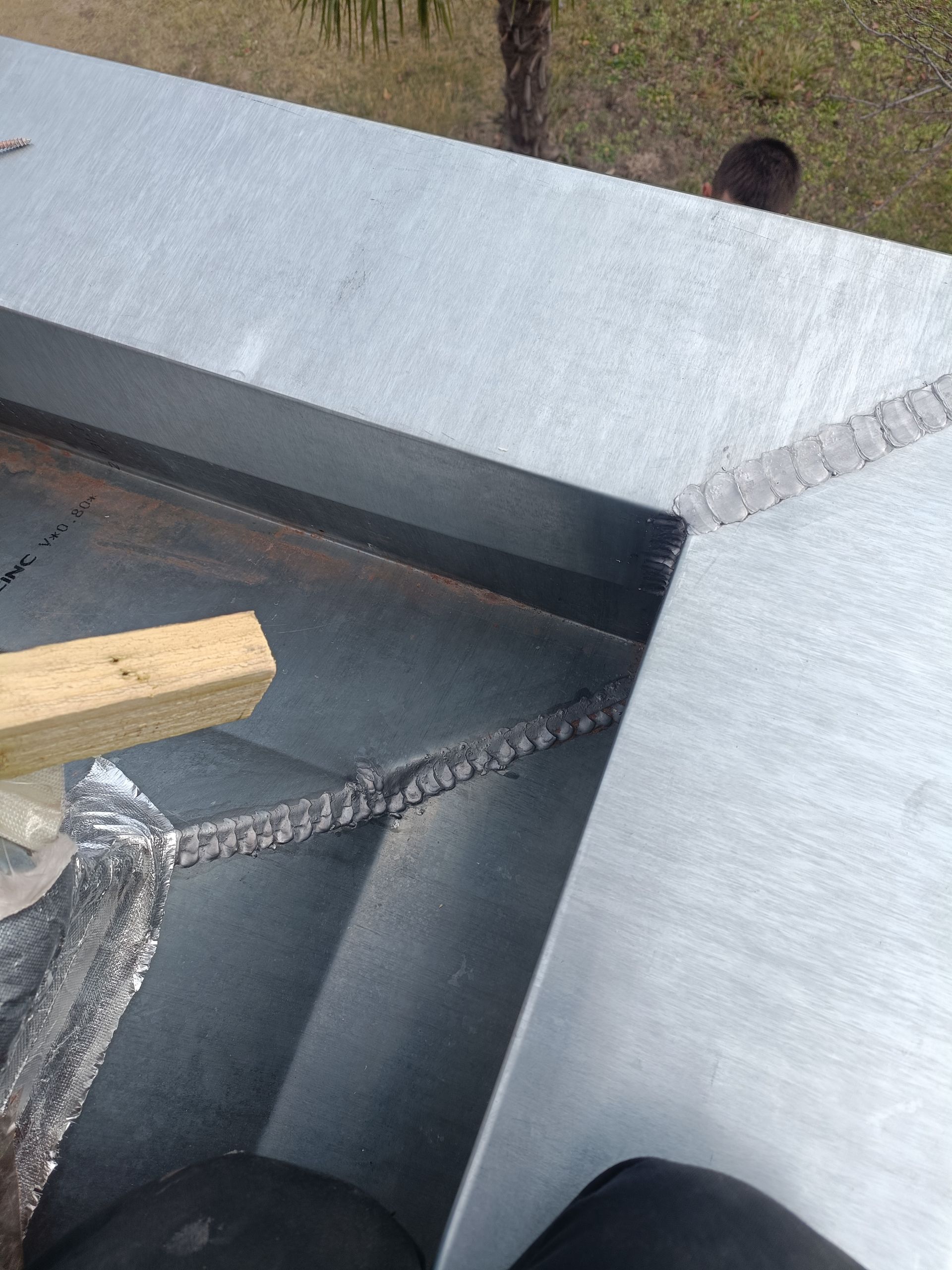 Gros plan sur une structure métallique grise à laquelle sont fixées une chaîne et une planche de bois, à l'extérieur.