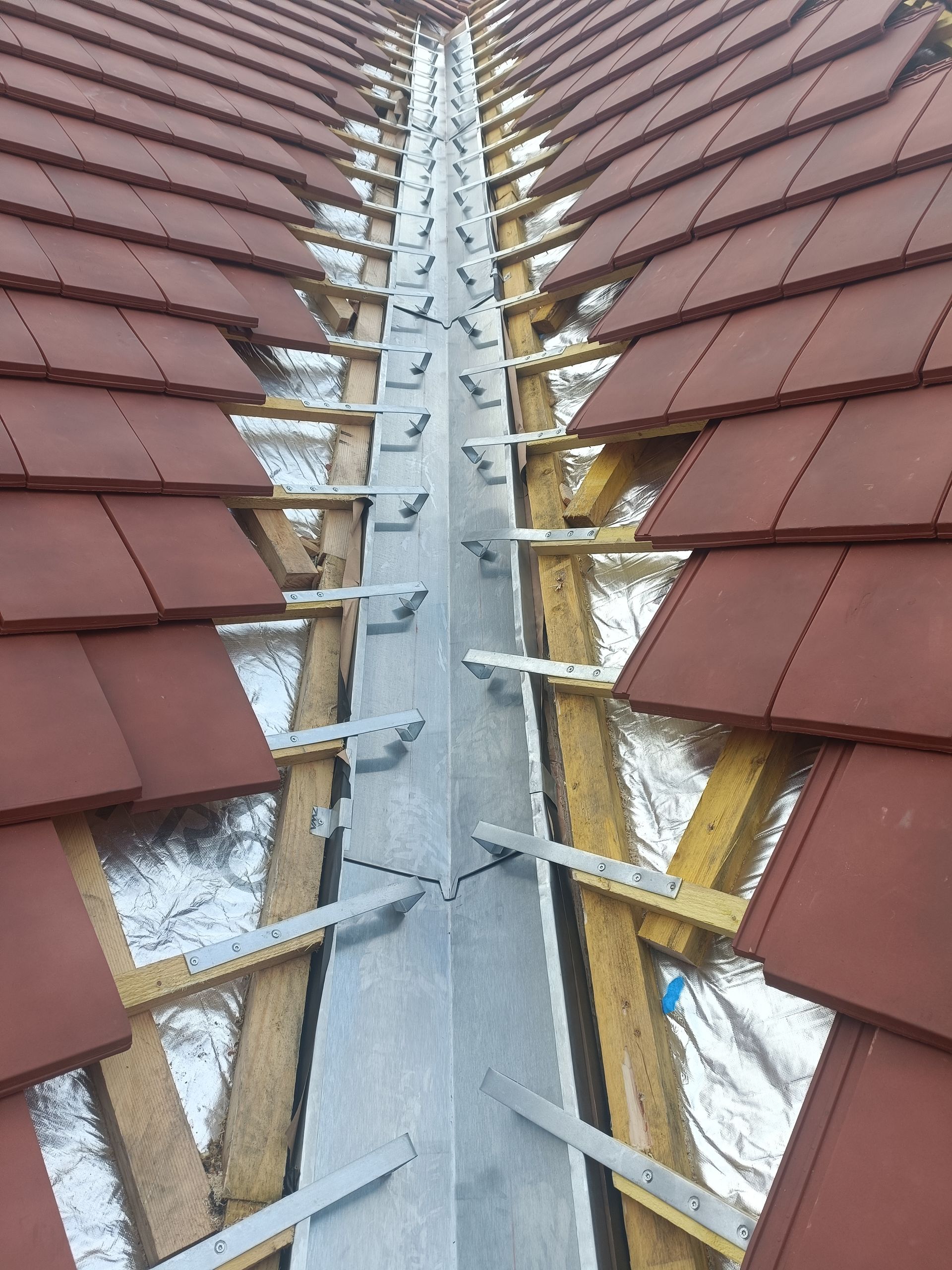 Noue de toit avec tuiles rouges et bande métallique centrale, montrant des travaux de construction en cours.