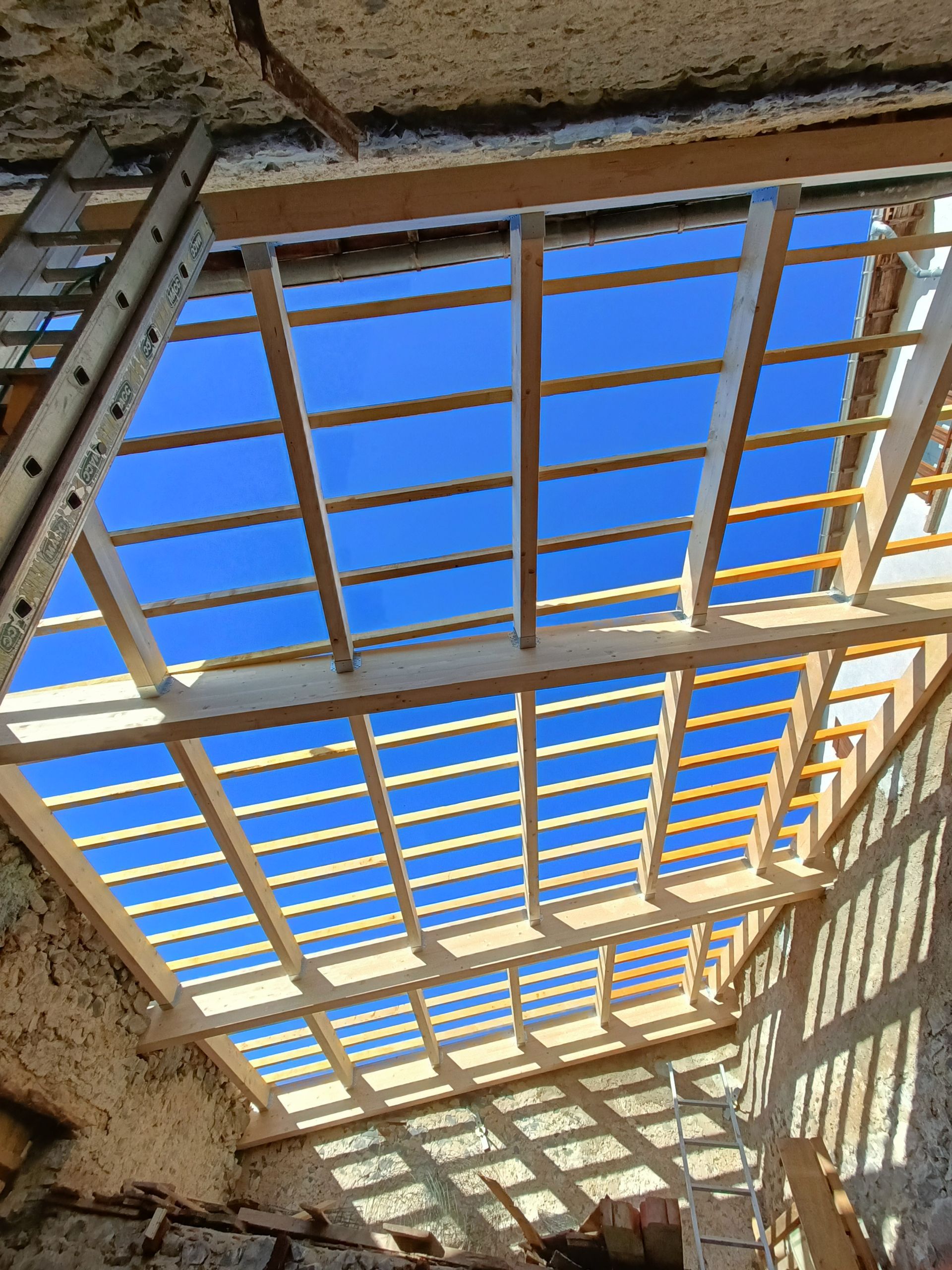 Toiture endommagée avec poutres en bois apparentes et ciel bleu visible à travers le plafond ouvert.