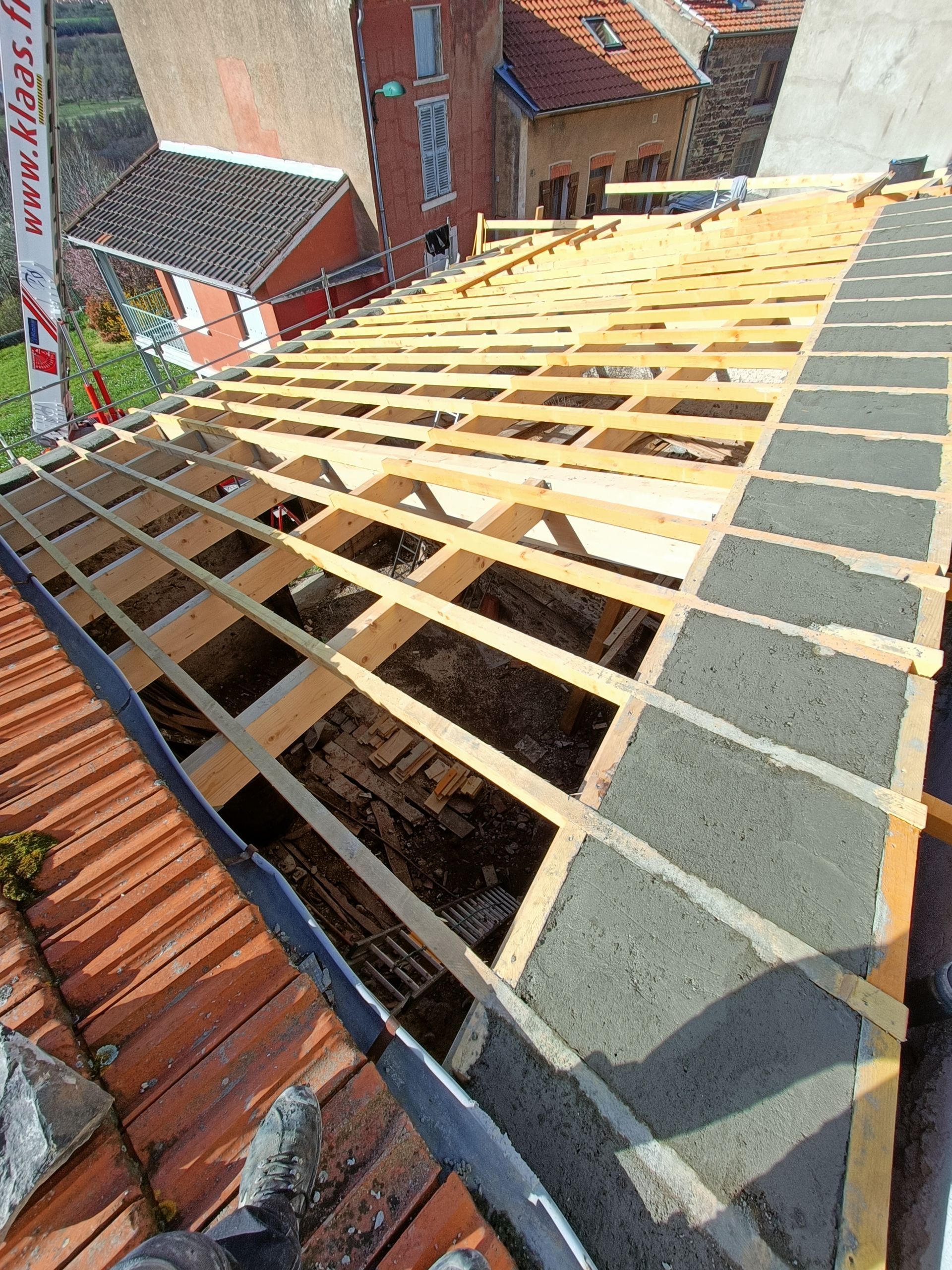 Toiture en construction avec chevrons en bois apparents et sous-toiture grise sur des maisons en briques.