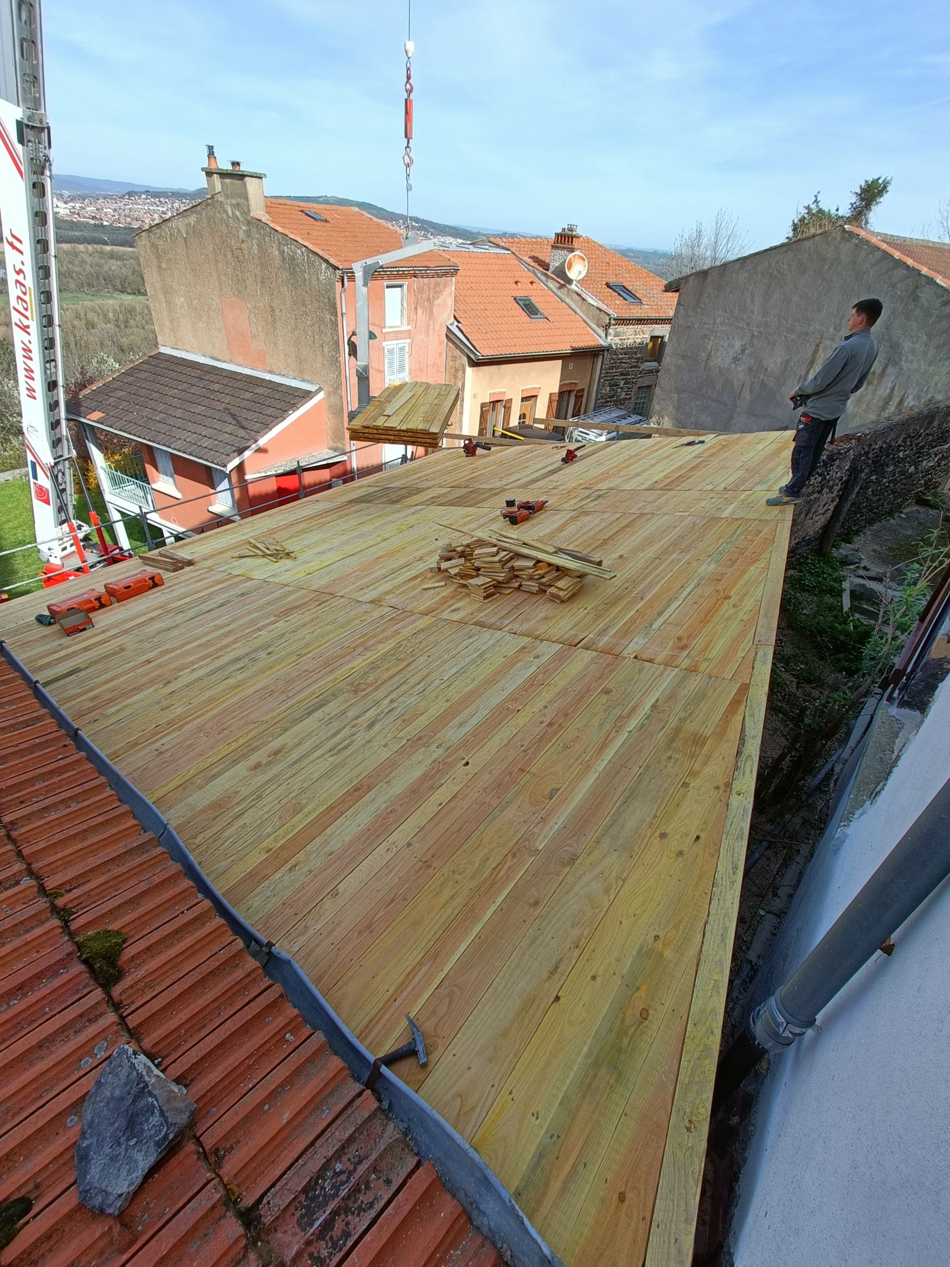 Couvreur sur un toit en pente, près de maisons aux tuiles rouges.