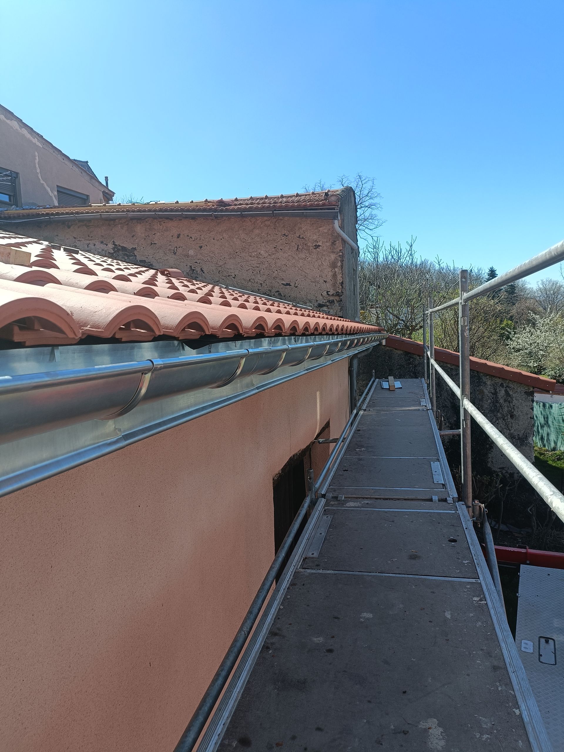 Étroite passerelle sur le toit, longeant un toit de tuiles en terre cuite.