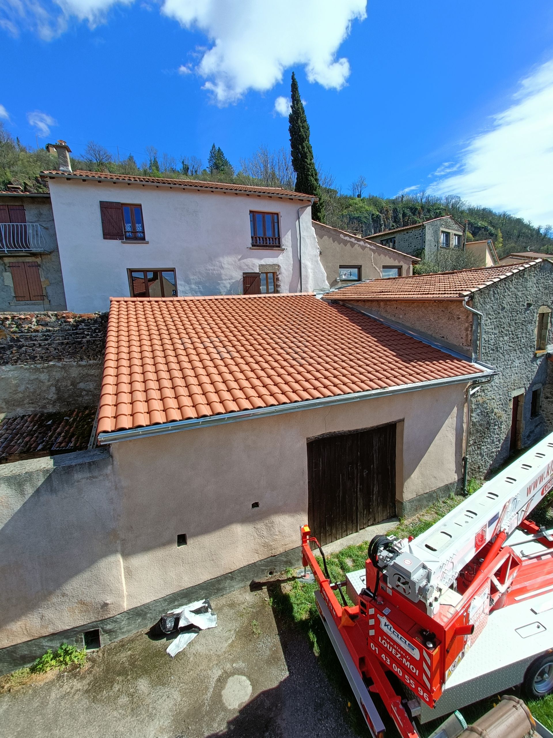 Un ascenseur de chantier rouge à côté d'une maison blanche aux toits de tuiles.