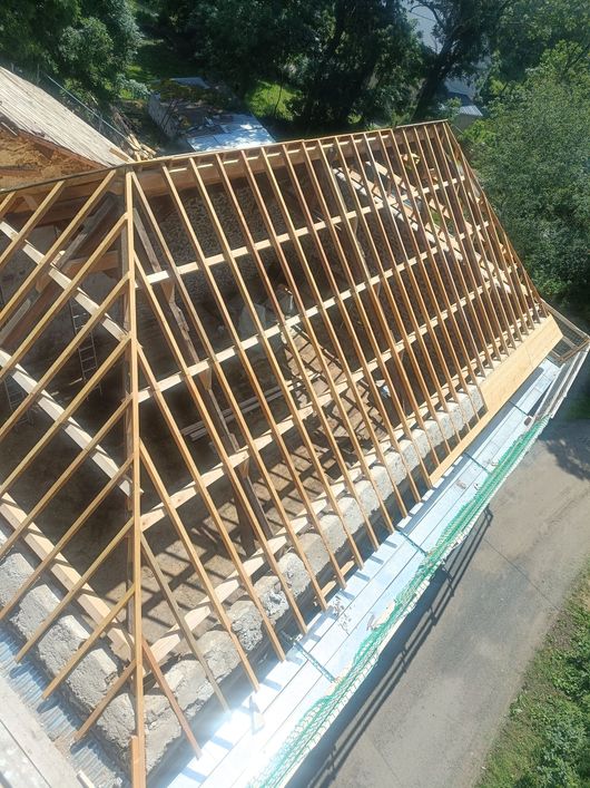 Charpentes de toit en bois disposées sur une longue structure à l'extérieur, au bord d'une route et d'une pente herbeuse.