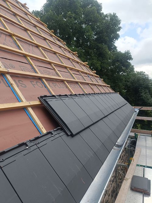 Toiture en construction avec bardeaux noirs installés sur une sous-couche apparente et des liteaux en bois.